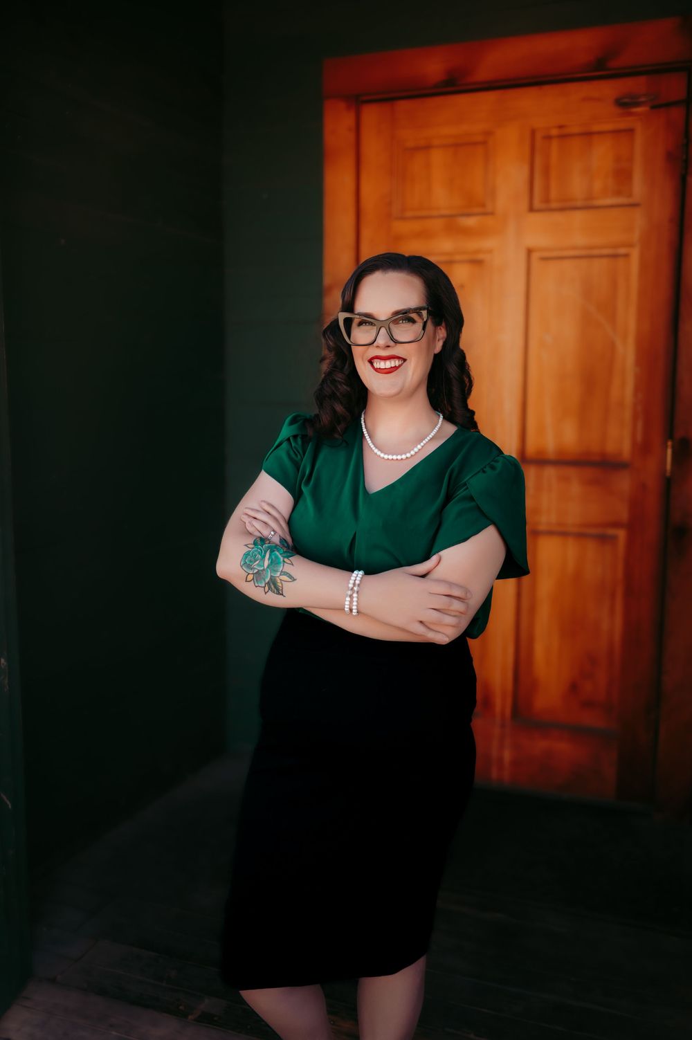 Person in green top and glasses sitting in dimly lit room with wooden doors.