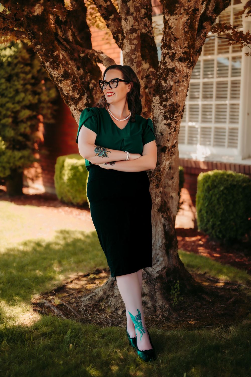Artistic outdoor photoshoot under a tree with dark dress and visible tattoos.