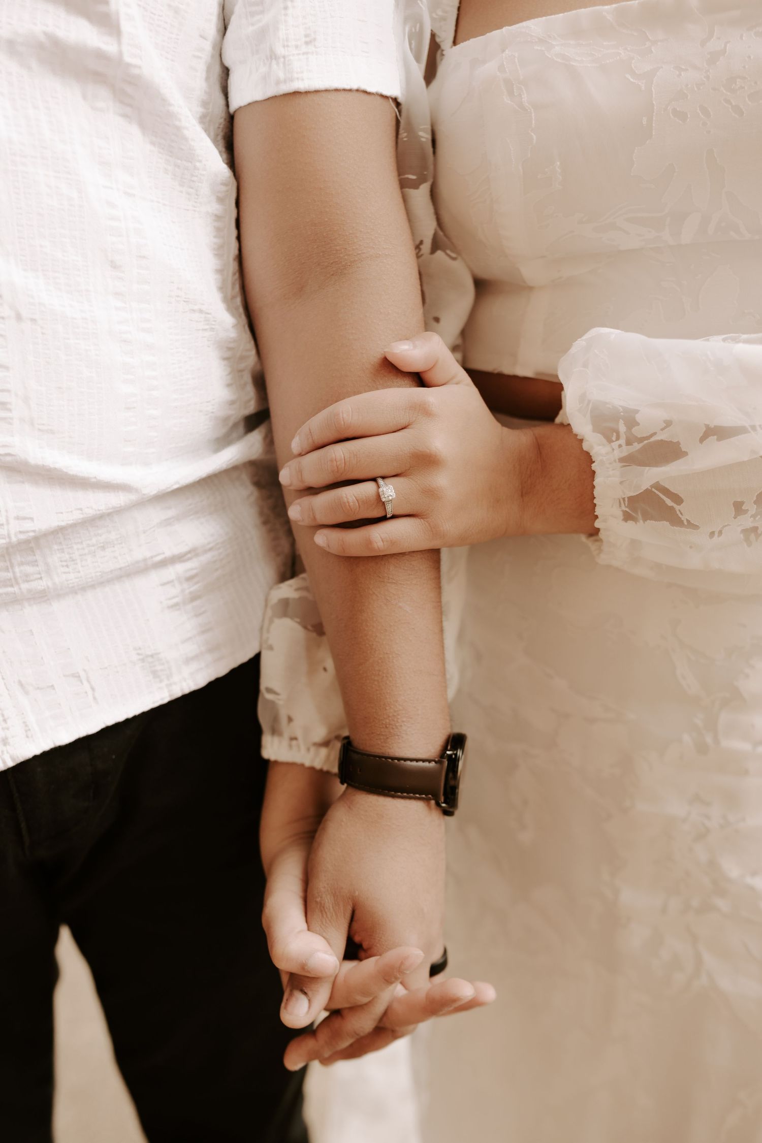 Close-up detail shot of hands and arms embracing in white attire.