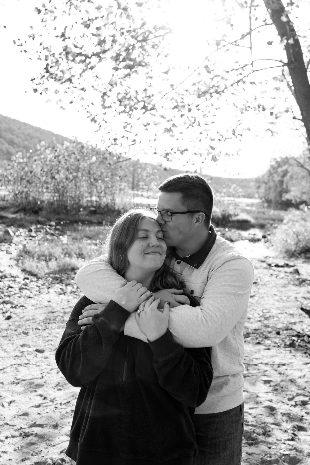 Black and white photo of couple embracing tenderly outdoors in an autumn landscape.