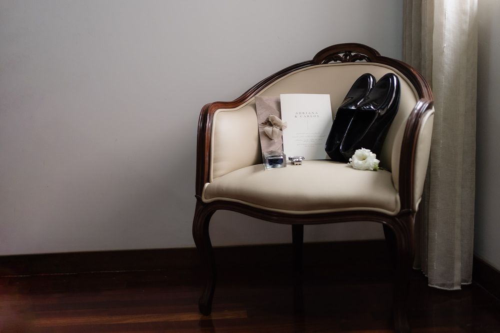 A vintage beige upholstered armchair with curved wooden frame sits elegantly against a dark wall.