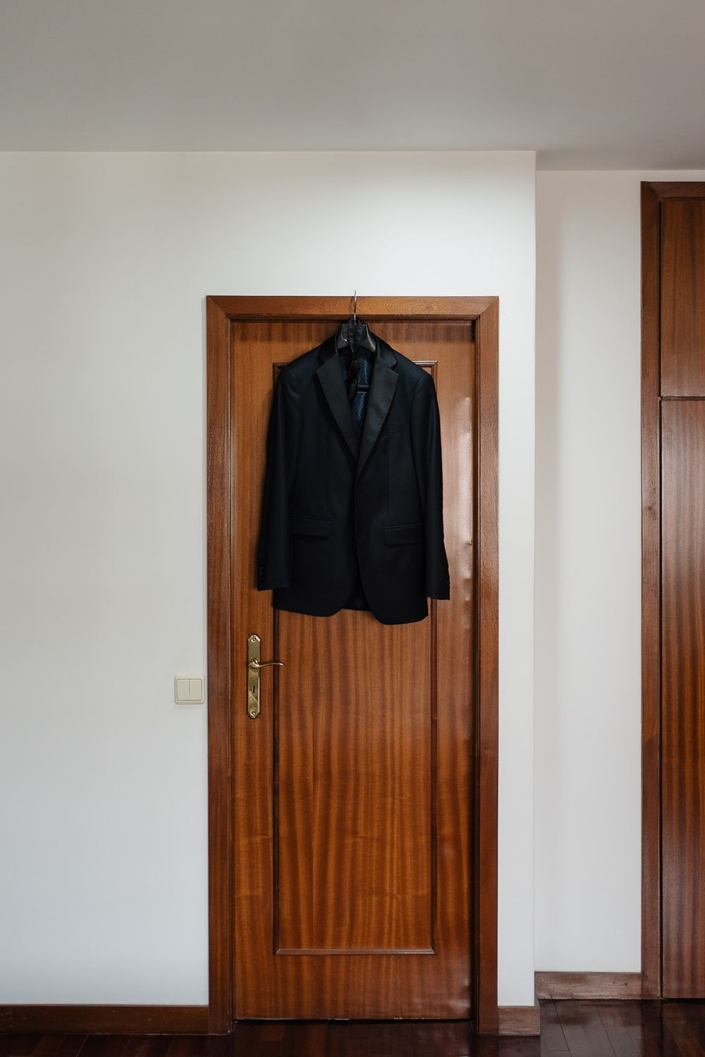 A black suit jacket hangs on a wooden door in a minimalist white interior hallway.