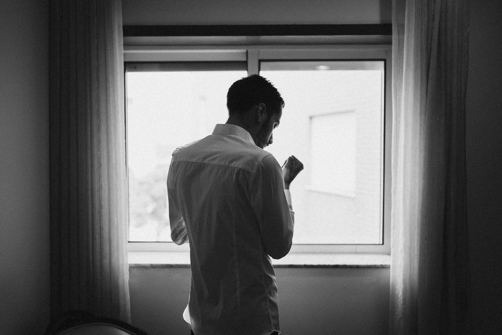 A person adjusts their tie while getting ready in front of a mirror in a dimly lit room.
