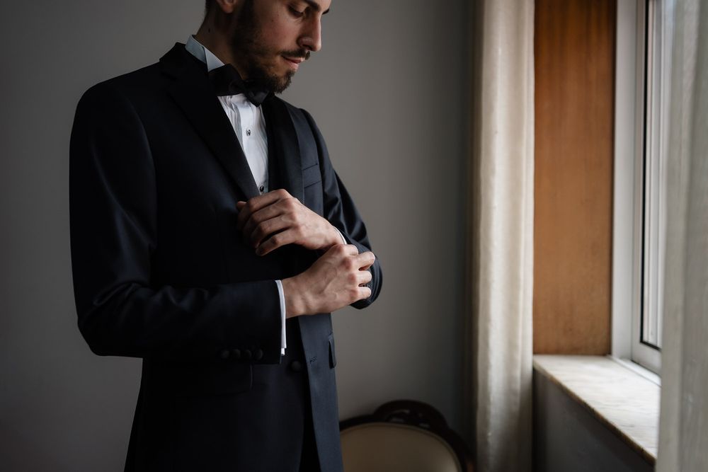 Three artistic black and white photos of someone in formal wear adjusting their clothing near a window.