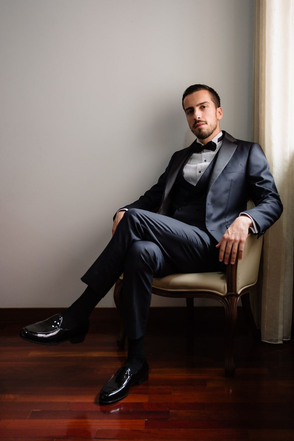 Professional portrait of someone in a dark suit lounging in a leather chair against a minimalist interior setting.
