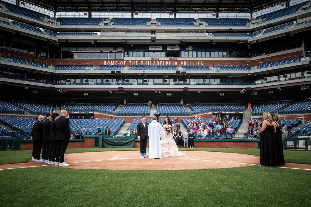 Panoramic view of an empty baseball stadium with wedding party arranged on the field for photos.