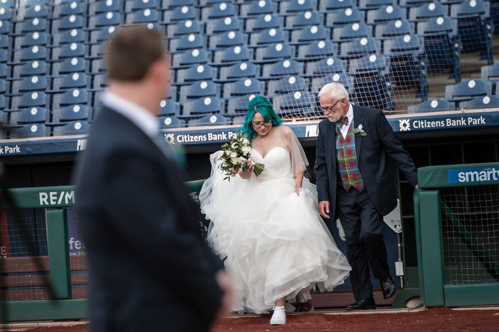 A bride and her father walk out of the Phillies home dugout to walk down the aisle to her groom for the ceremony.