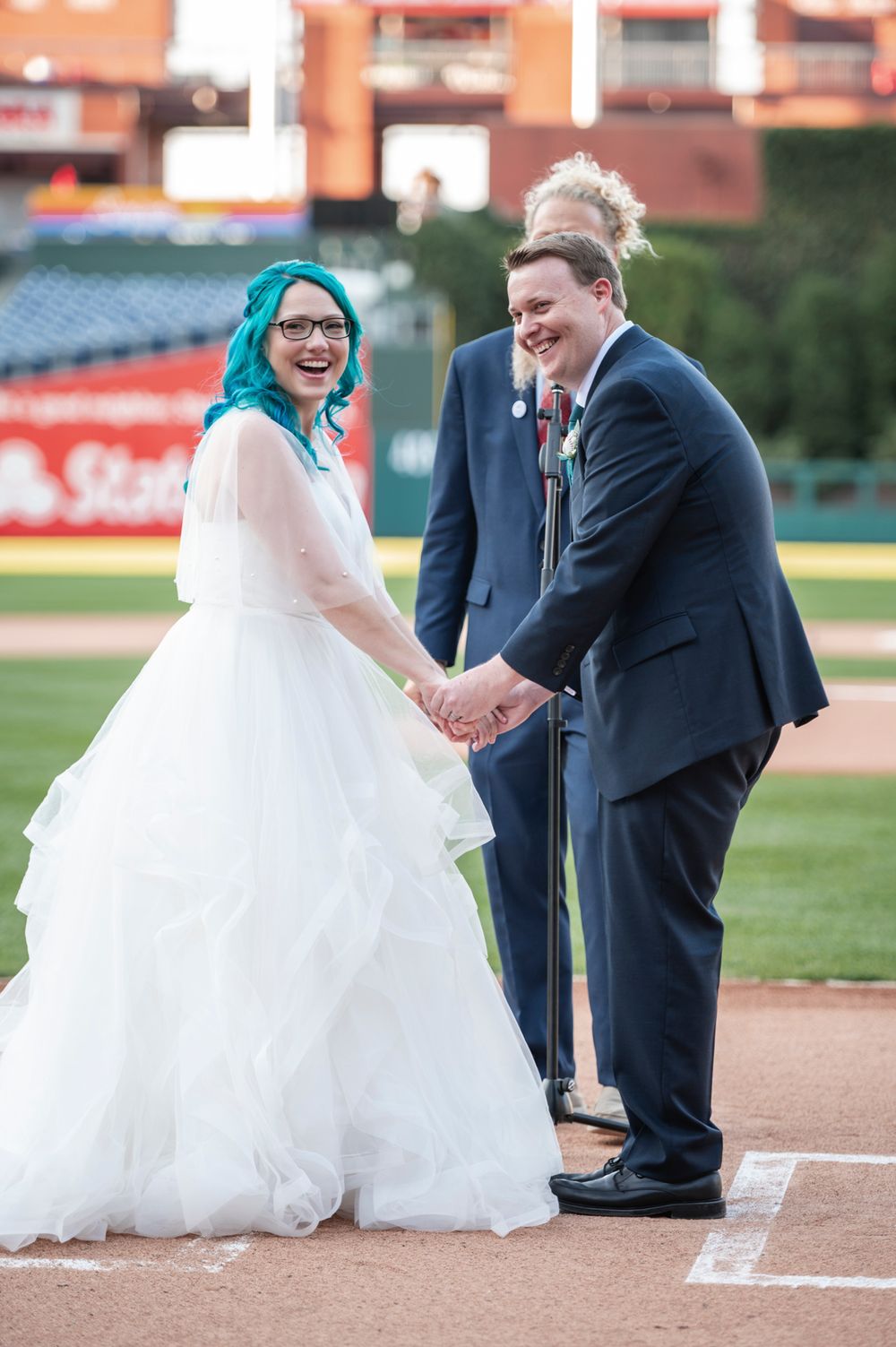 A wedding couple shares a playful moment at home plate on a baseball field during their special day.