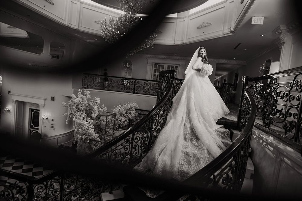 A romantic wedding photoshoot in a dimly lit grand ballroom with elegant chandeliers and ornate decor.