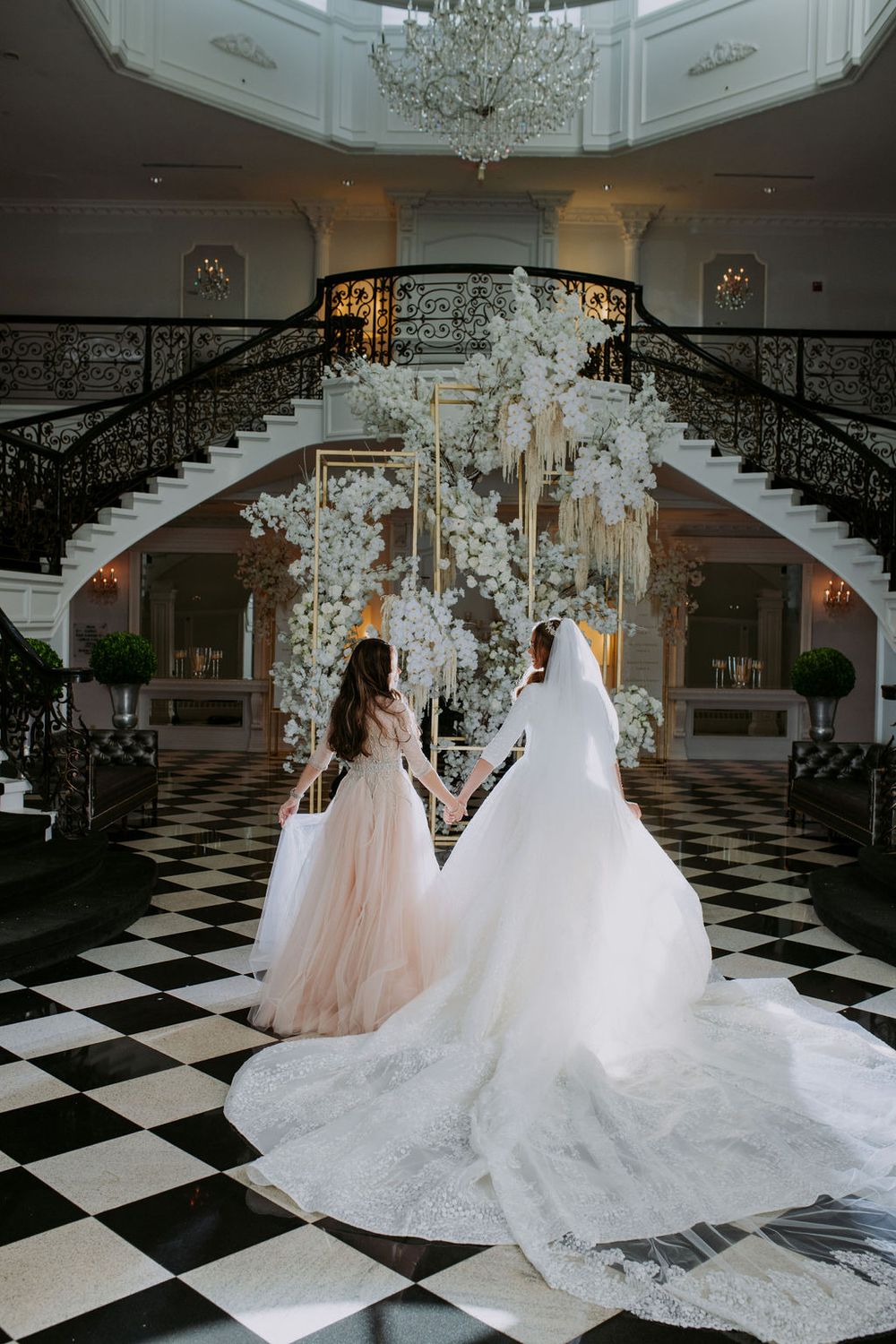 Elegant wedding venue with black and white checkered floor and grand staircase decorated with white floral arrangements.