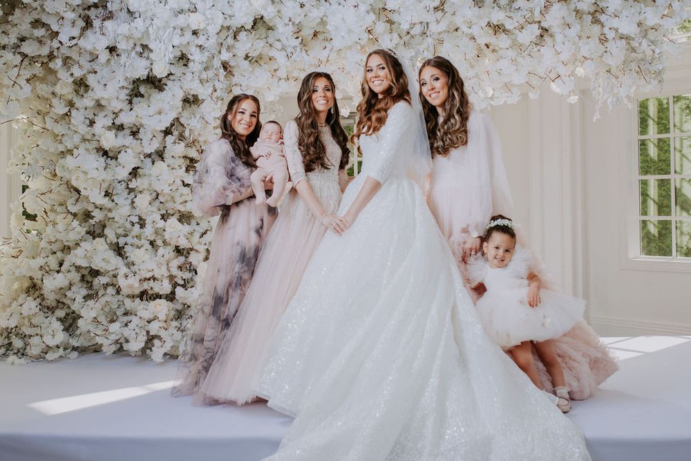 A bridal party in soft pastel gowns poses together against a stunning floral wall backdrop.