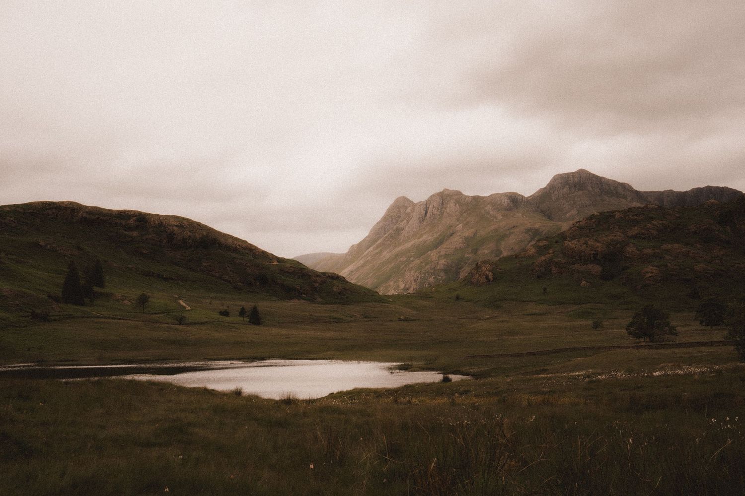 A panoramic view of the Scottish Highlands shows rugged mountains and a serene loch under moody skies.