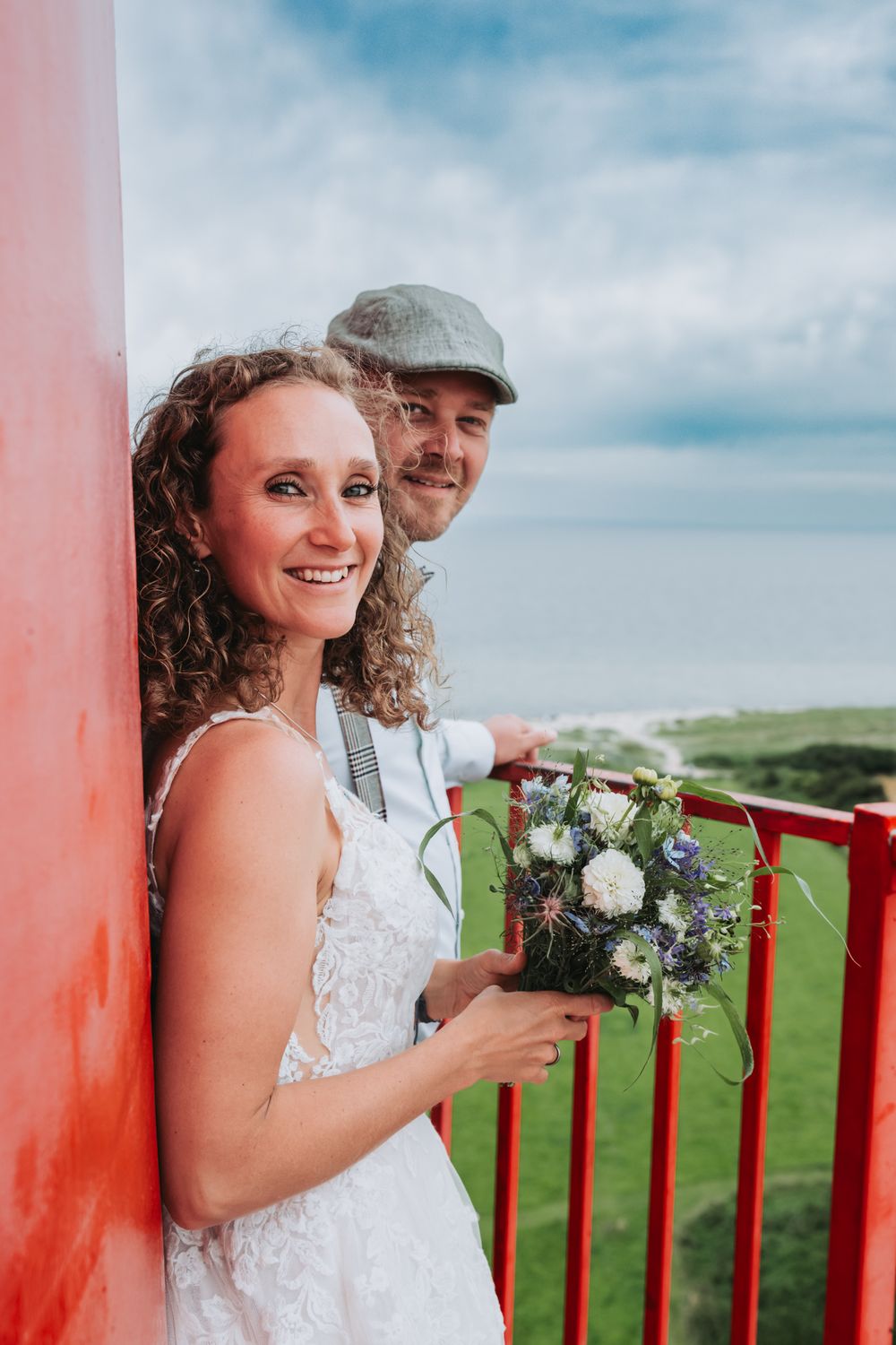 A couple shares a romantic moment on a balcony overlooking green coastal hills on their wedding day.