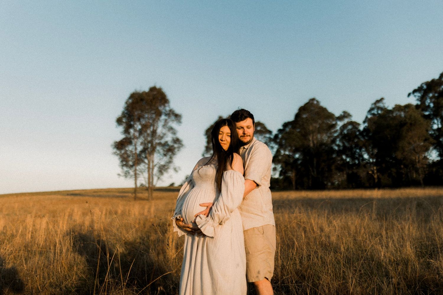 Romantic couple embracing in rustic field during golden sunset.