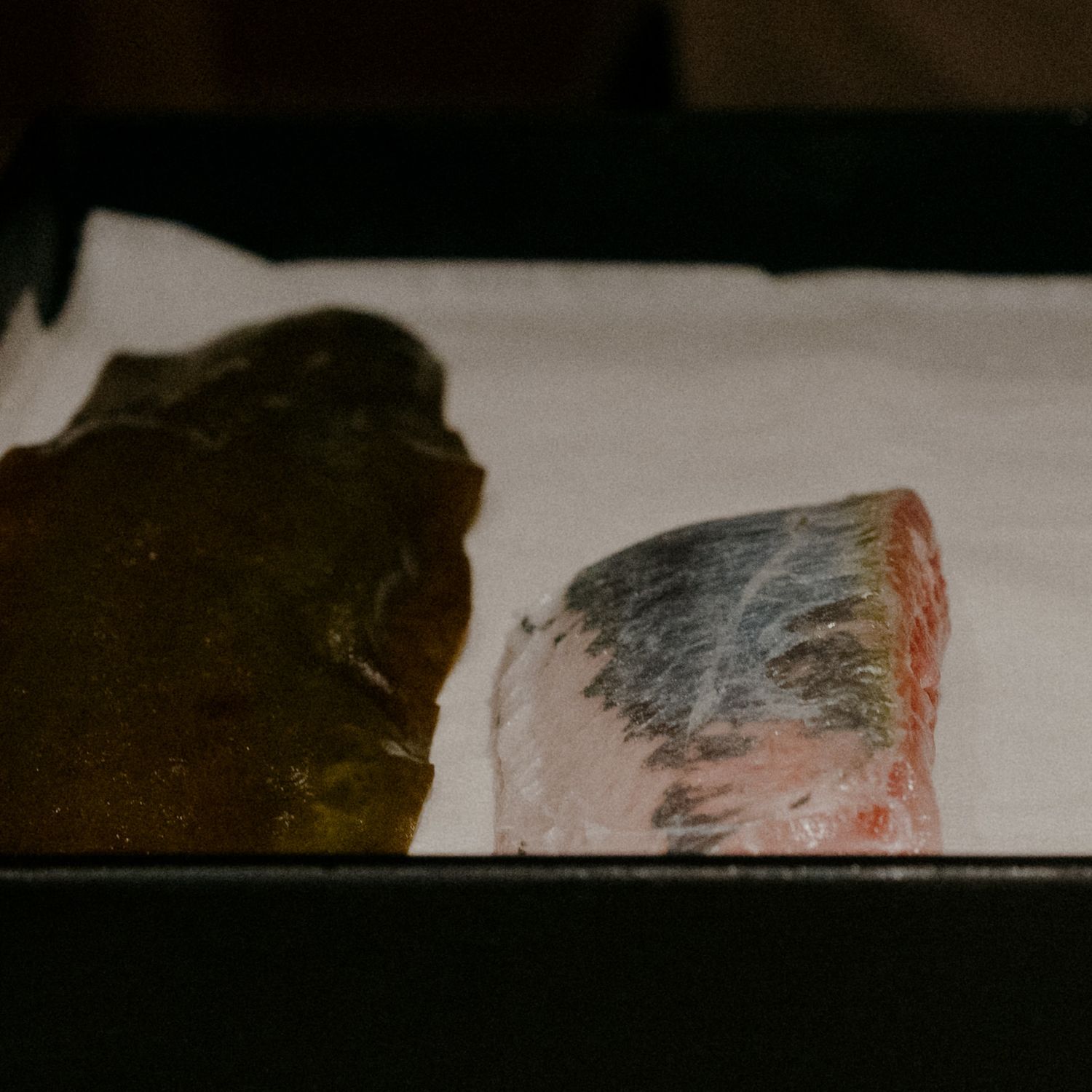 Raw fish fillets arranged on a white surface in preparation for sushi making.