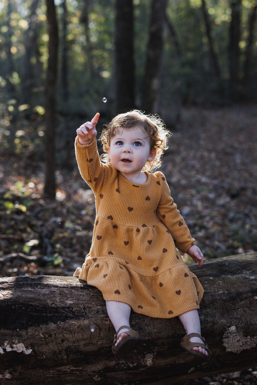 A toddler exploring a forest trail while parents watch affectionately in the background. Raw and authentic Snohomish family lifestyle
