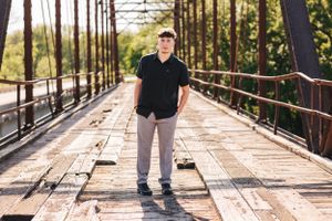 Person walking on wooden bridge pathway surrounded by tall trees and natural lighting.