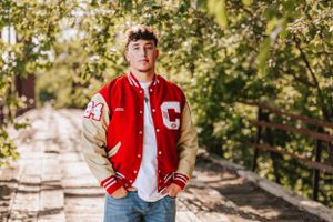 Person wearing red varsity jacket poses during outdoor portrait session.