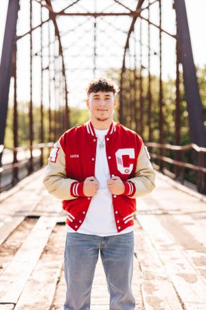 Person in red and white varsity jacket poses on wooden bridge during golden hour.