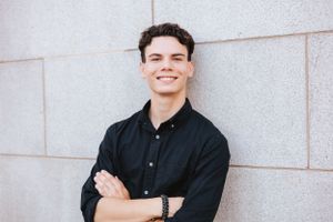 Individual in black shirt poses against white wall in outdoor portrait series.