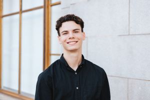 Portrait subject in dark button-up shirt standing near modern architecture.