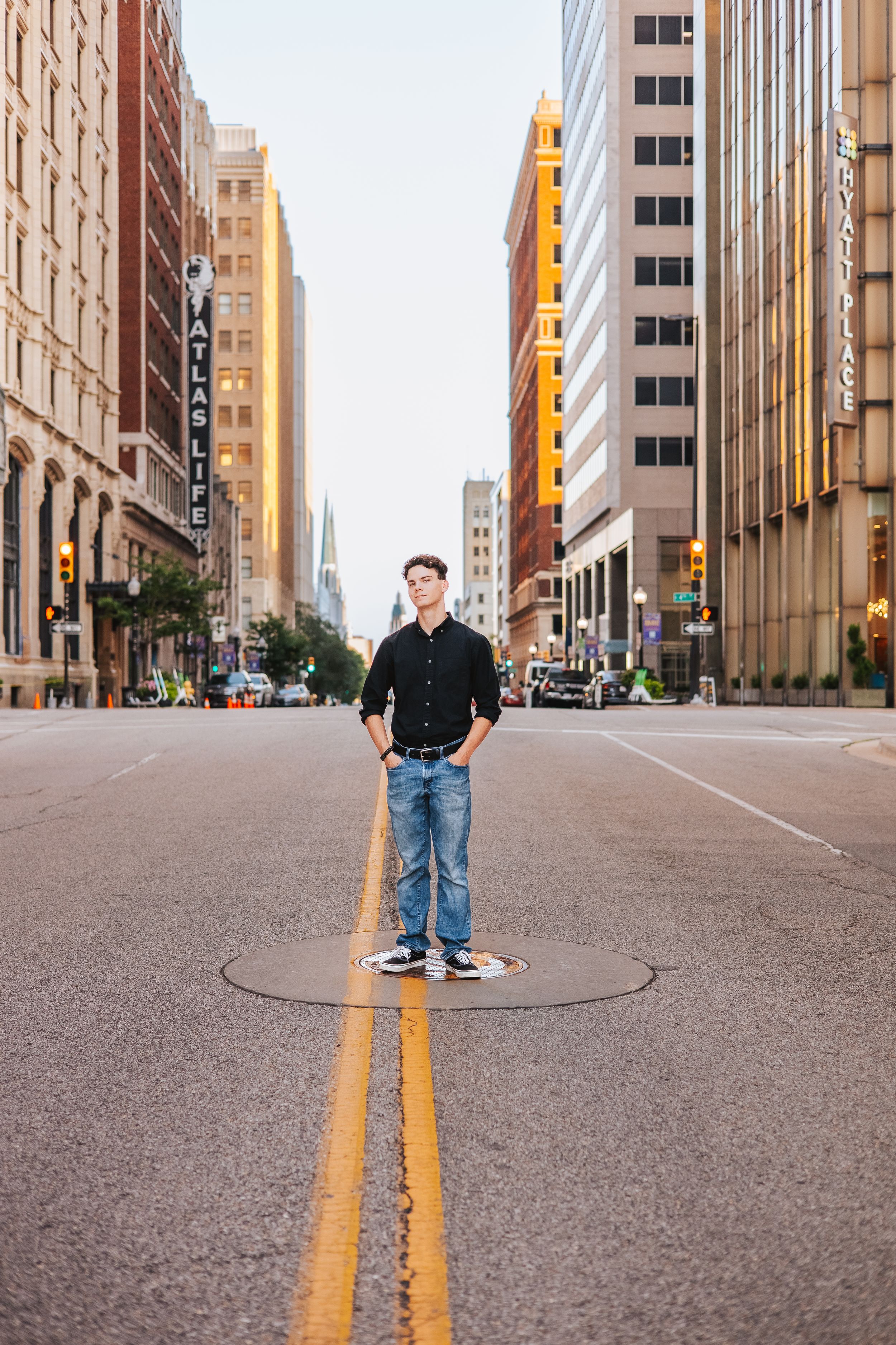 Person standing in middle of empty city street with tall buildings and yellow lines.