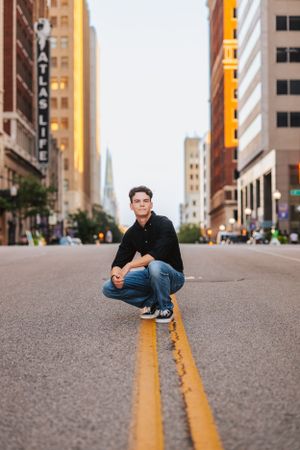 Urban street photography series showing person sitting on yellow road lines with city buildings in background.