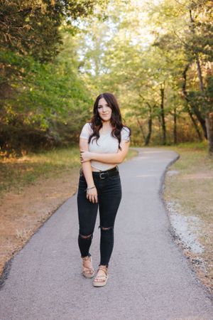 Fashion portraits on a gravel path surrounded by lush green trees.