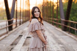 Romantic portrait session in flowing dress on rustic bridge during sunset.
