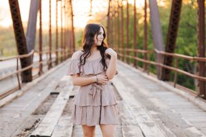 Ethereal photography in ruffled dress with golden hour lighting on wooden bridge.