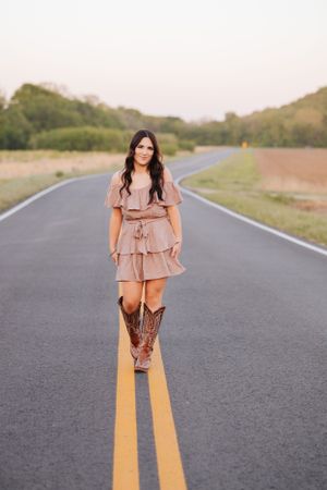 Woman in pink dress stands on yellow lines of empty rural road.
