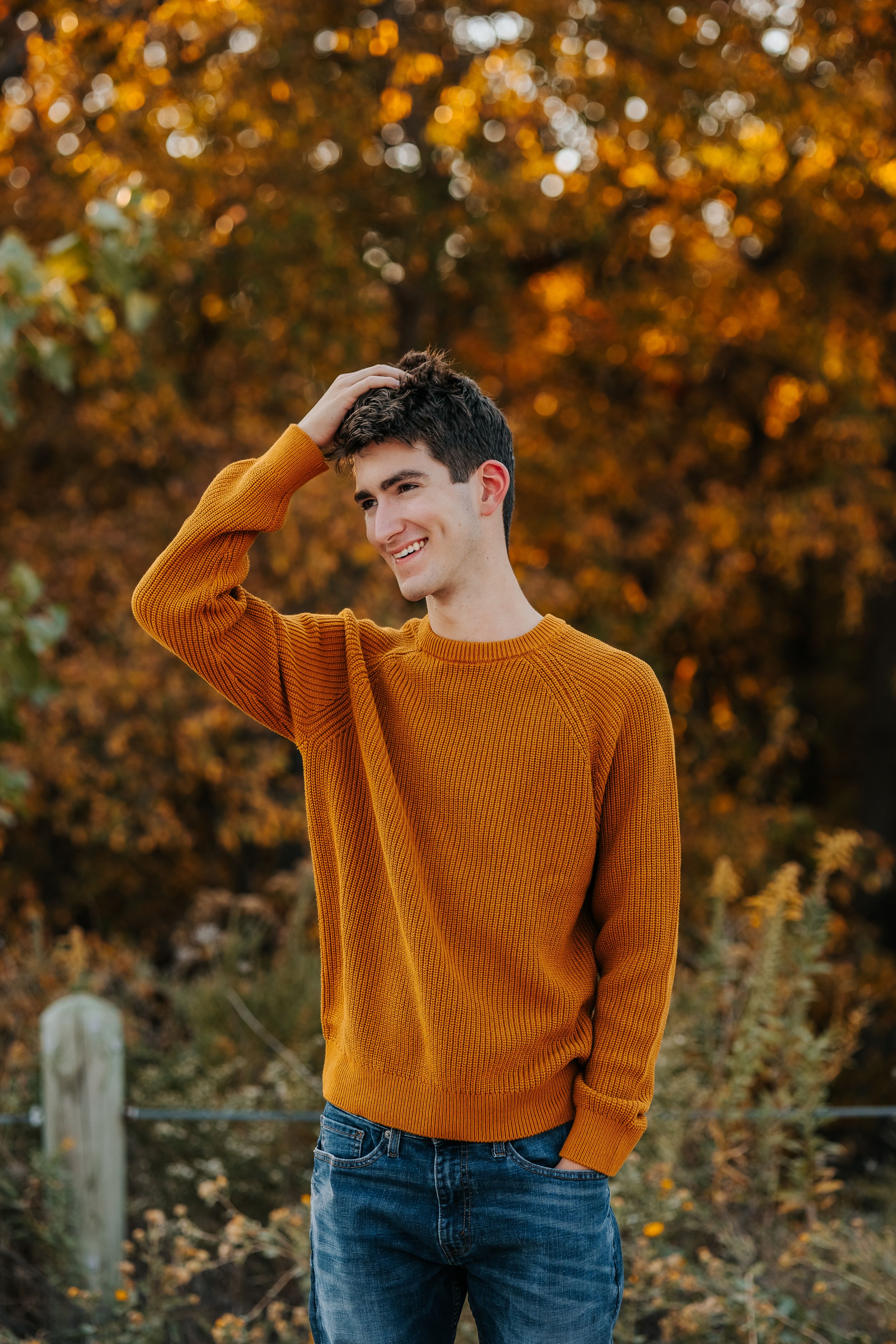 Figure in bright orange sweater poses against autumn foliage background.