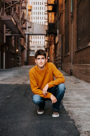 Person in mustard sweater crouching in urban alleyway during photo session.