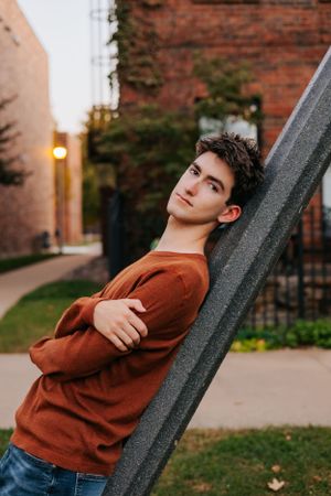 Person in brown sweater leaning against diagonal beam in urban setting.