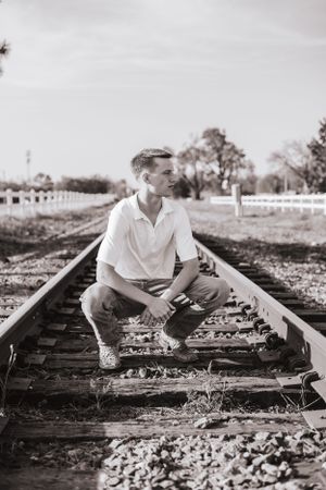 Black and white photo of person sitting on railroad tracks in casual attire.