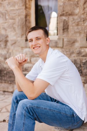 Person in casual white t-shirt and jeans poses against stone wall.