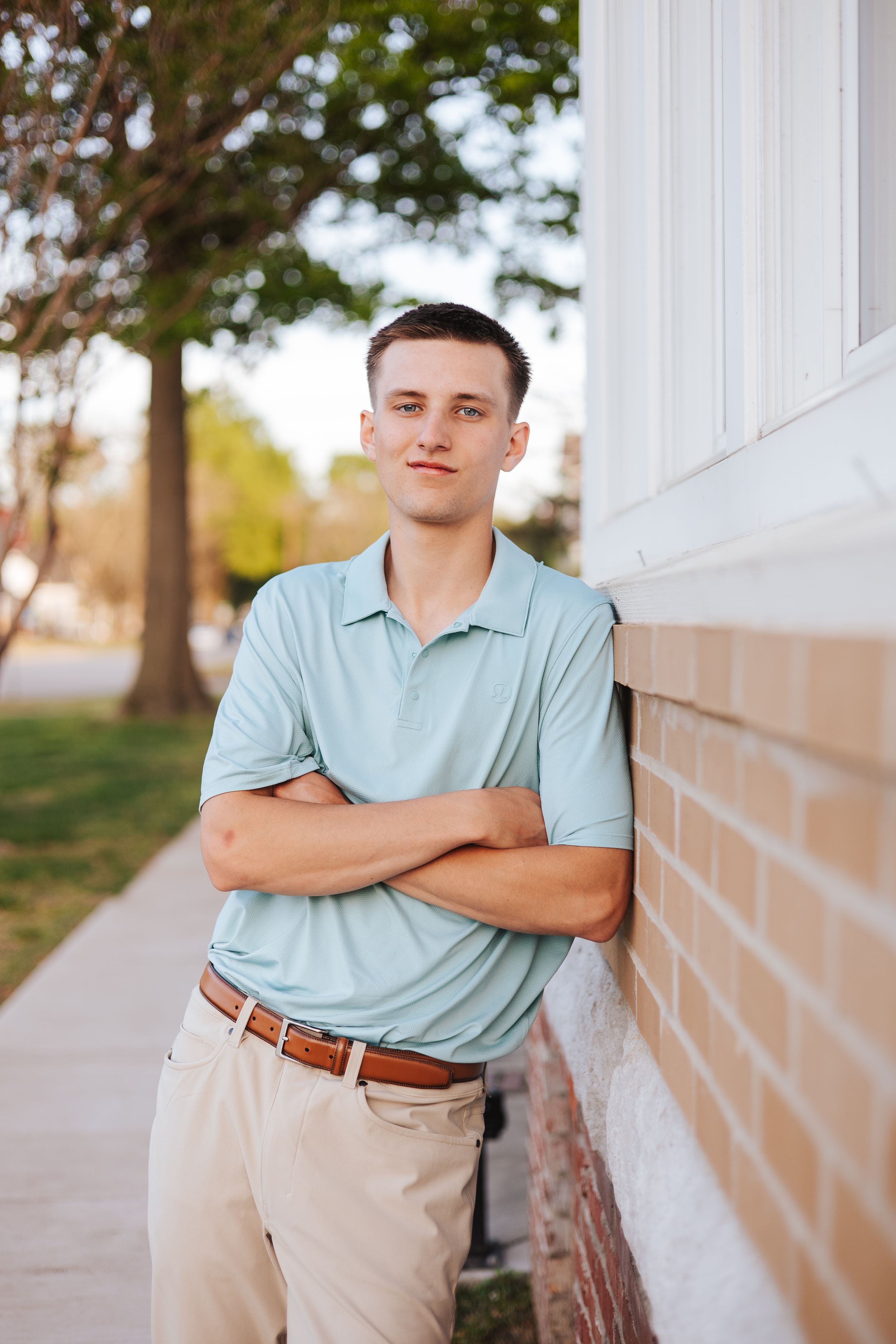 Person in light blue polo leans against white wall outdoors.