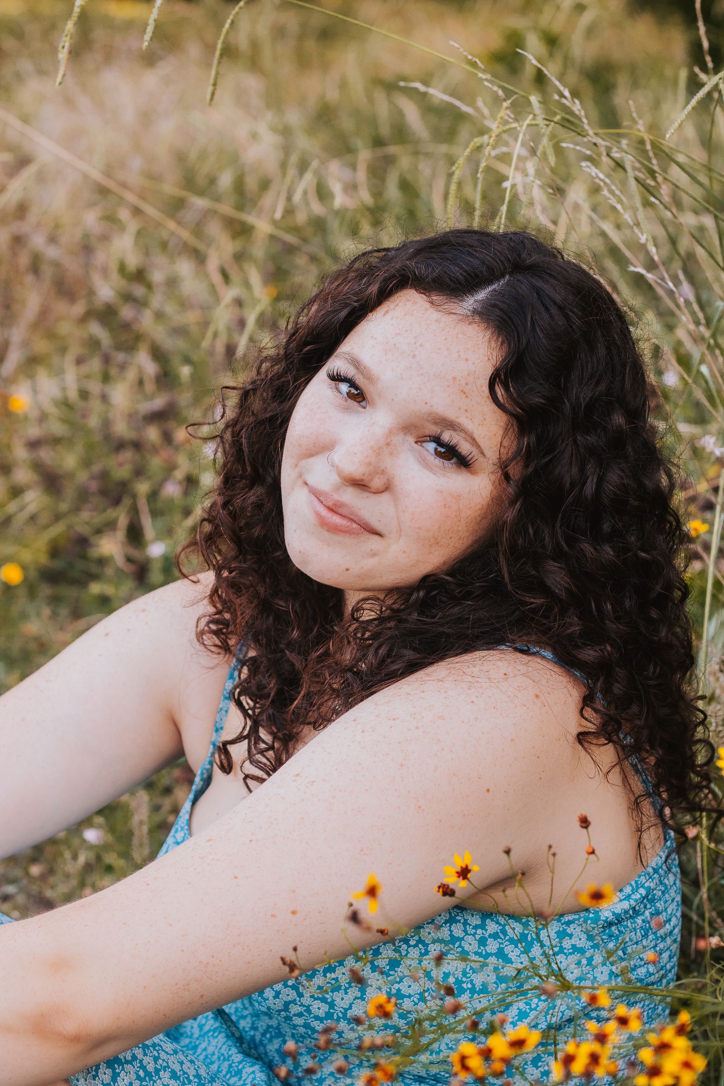 Portrait in blue dress lying among wildflowers during golden hour.