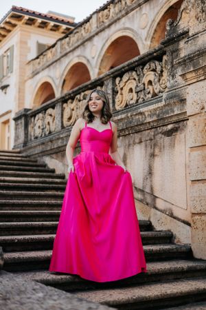 A vibrant pink ballgown creates stunning contrast against historic stone steps and architecture.