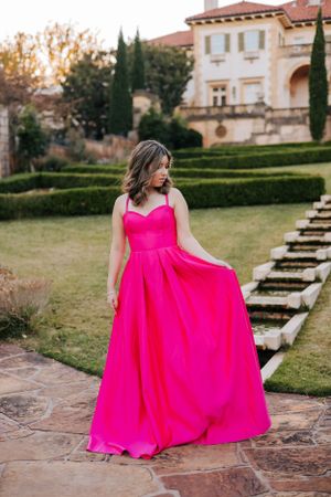 A flowing hot pink gown twirls gracefully on stone steps near a Mediterranean-style villa.