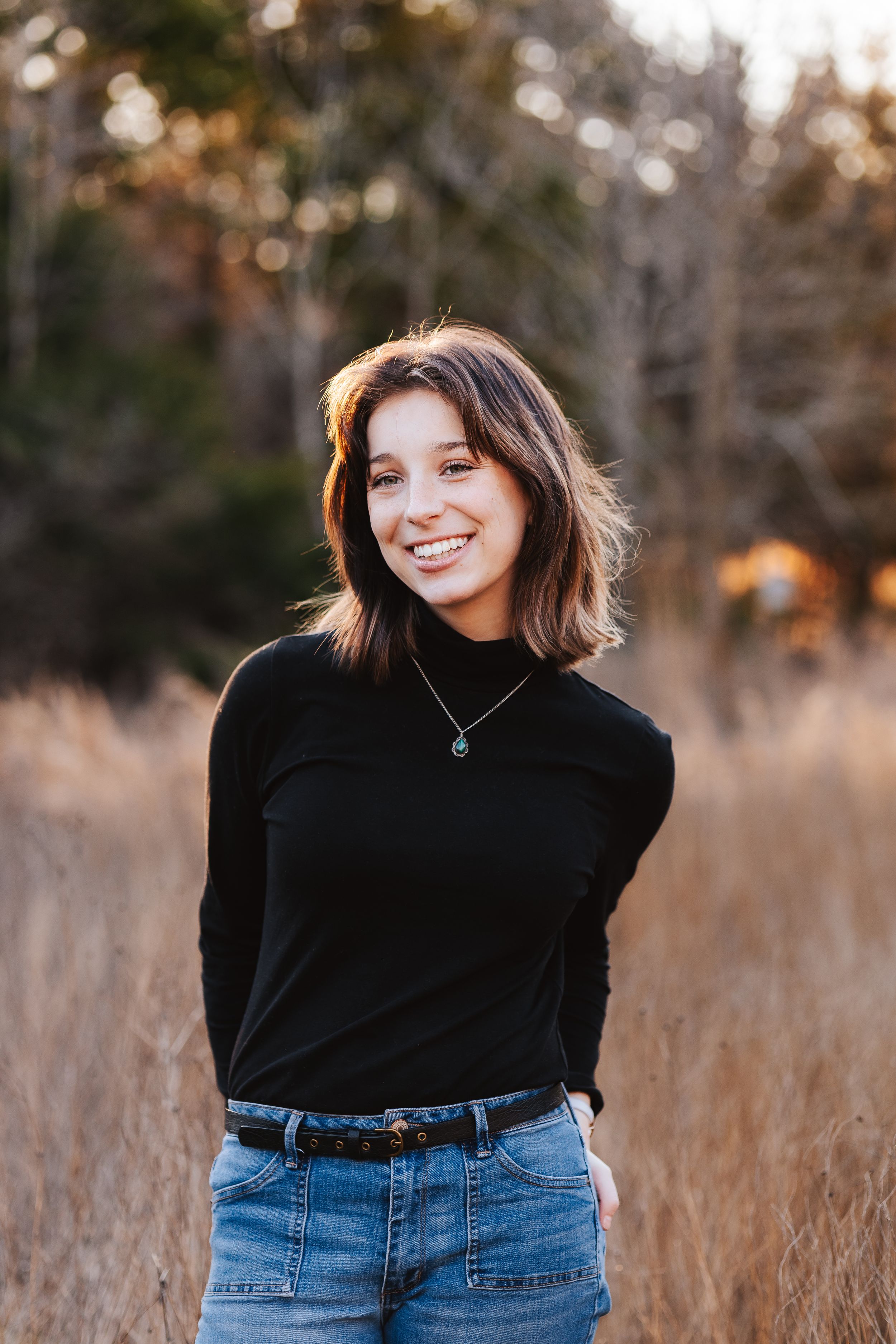 Woman in black turtleneck and jeans poses in golden field at sunset.