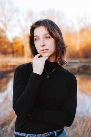 Moody portrait series in black turtleneck against autumn landscape with reflective water.