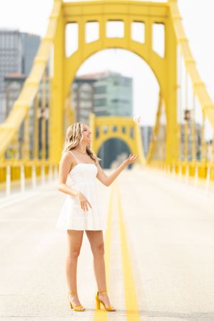 Figure in white dress poses on iconic yellow bridge with cityscape backdrop.