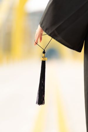 A graduation tassel hanging from black academic regalia against a blurred background.