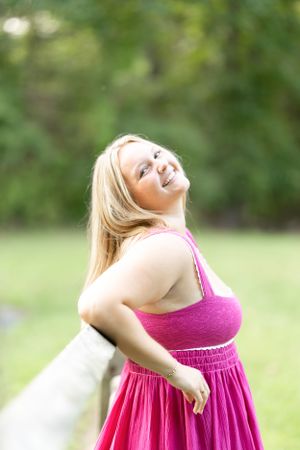 A joyful portrait in a pink dress against a soft green natural background.