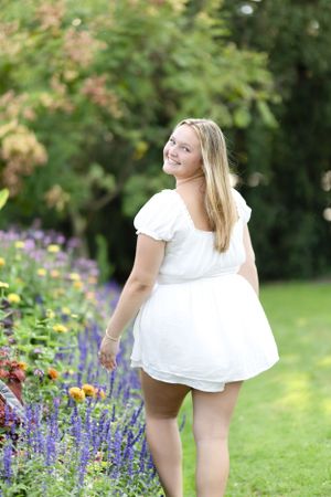 White dress flowing in a garden setting with purple and colorful flowers.