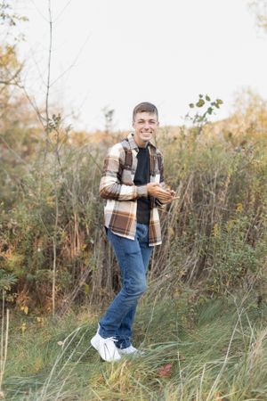 Child in plaid shirt and jeans plays in tall autumn grass.