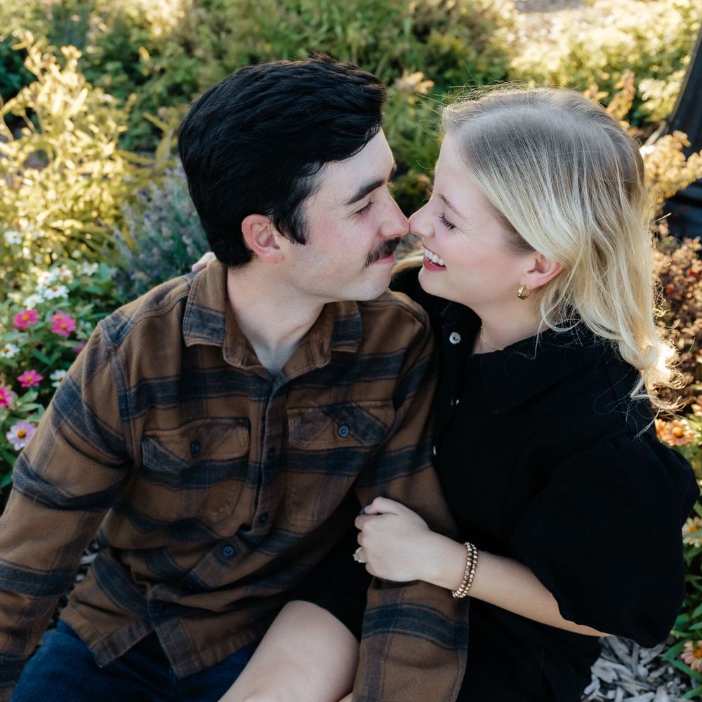 A couple shares an intimate moment outdoors during golden hour among blooming flowers.