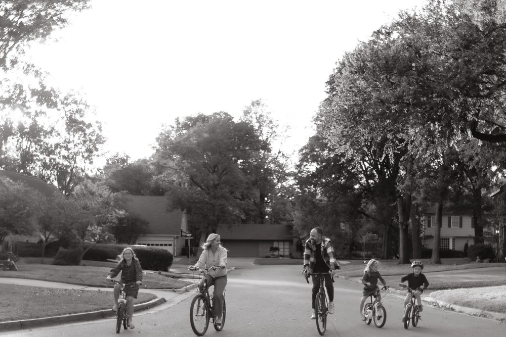 Black and white photograph of five cyclists riding together down a residential street.