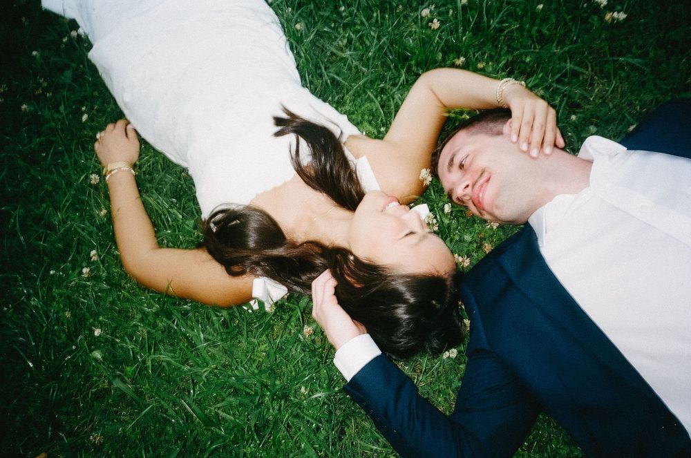 Two people lying on green grass wearing white and navy clothing viewed from above.